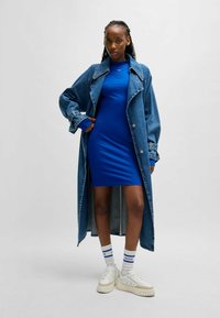 Denim lange jas met brede kraag over een aansluitende blauwe jurk. Platform sneakers en witte sokken met blauwe accenten. Eenvoudig ontwerp, casual stijl.