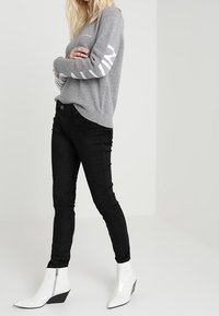 Grå stickad tröja med vit logodetalj på ärmarna, kombinerad med svarta smala jeans och vita ankelboots med dragkedja.