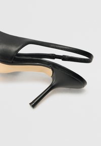 Musta nahkainen korkokengät, joissa on terävä kärki ja ohut korko, slingback-malli ja hieman teksturoitu pinta.
