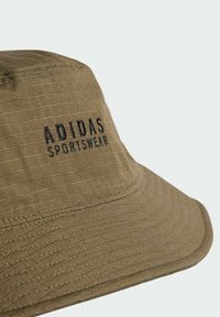 Brown bucket hat made of textured fabric featuring embroidered "ADIDAS SPORTSWEAR" logo in black, with a wide, sloping brim.