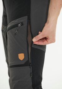 Zwarte en grijze broek met een ritsmesh zak en een leren logo patch. De stof is duurzaam met een mix van texturen.