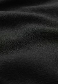 Tessuto nero con una superficie morbida e strutturata e leggere ondulazioni, che mette in risalto una finitura liscia e una profondità di colore.