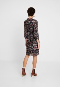 Robe fleurie avec un fond noir, à manches longues, taille cintrée et ourlet à mi-genoux. Associée à des bottines à talons bruns.