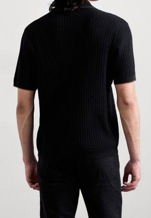 Schwarzes, geripptes Polohemd mit kurzen Ärmeln und einem dezenten Kragenrand, das aus einem strukturierten Stoff besteht. Ansicht von hinten.