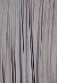 Gros plan sur un tissu doux gris clair avec de fines plis verticaux créant une texture et des ombres.