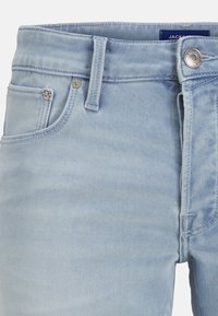 Jean en denim bleu clair en gros plan montrant la poche avant, les passants de ceinture, le bouton et une partie de la zone de la fermeture éclair.