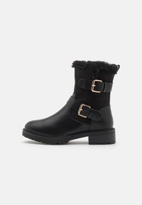 Bottes noires à la cheville en cuir et en suède, avec un parement en fausse fourrure, des accents à double boucle et une semelle en caoutchouc texturé.