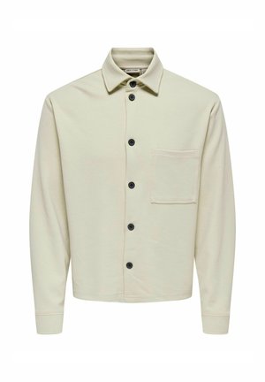 Lys beige skjorte med knapper lavet af struktureret stof, med krave, sorte knapper og en lomme foran. Lange ærmer med manchetter.