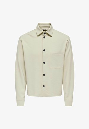 Jasno beżowa koszula na guziki wykonana z teksturowanej tkaniny, z kołnierzykiem, czarnymi guzikami i kieszenią z przodu. Długie rękawy z mankietami.