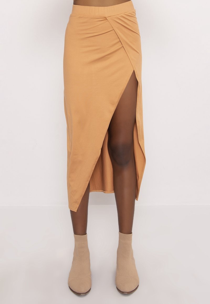 Mujer vistiendo una falda midi color beige con una abertura frontal, combinada con botines tobilleros de estilo calcetín en un fondo liso.