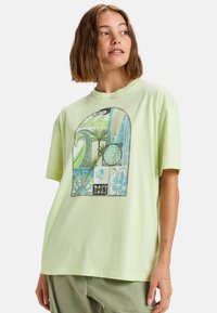 Camiseta de algodón verde claro con un estampado gráfico colorido de palmeras y patrones. Corte holgado, mangas cortas, escote redondo.