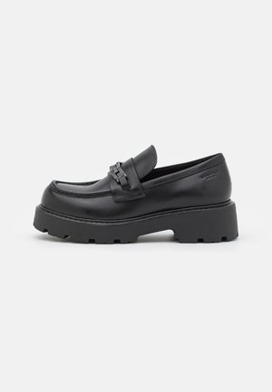 Sort læderloafer med kraftig rillesål og dekorativ metalspænde på skaftet, vist i sideprofil på hvid baggrund.