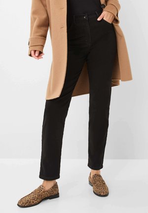 Pantalon noir à coupe décontractée, associé à un manteau en laine beige. Les chaussures sont beiges avec un imprimé léopard. Textures lisses et designs simples.