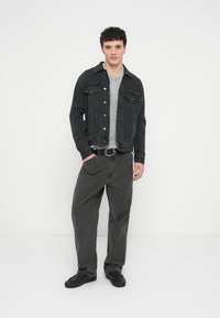 Crna traper jakna preko sive majice, uparena s sivim hlačama na pruge i crnim cipelama. Odjevna kombinacija odražava ležeran i opušten stil.