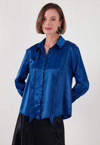 Blue satin blouse with a collared design, long sleeves, and vertical pleats on the front. Smooth texture; casual fit.