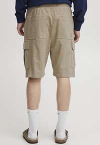 Bermudas cargo color caqui con una cinturilla elástica, cuatro bolsillos y un tejido duradero. Calcetines y sandalias visibles en la parte inferior.