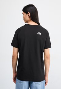 Camiseta de algodón negra con cuello redondo y mangas cortas. Presenta un pequeño logo blanco en la parte superior de la espalda. Corte informal, textura suave.