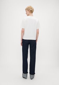 Hvit t-skjorte med korte ermer sammen med mørkeblå vidde jeans med oppbrettede ermer og denimdetaljer. Enkel design med minimal detaljering.