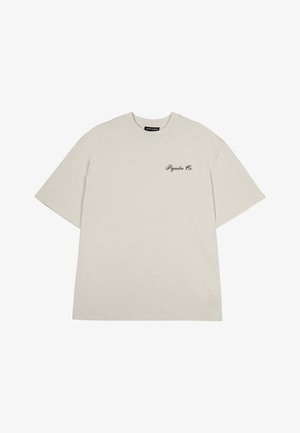 Ljusbeige oversized t-shirt, korta ärmar, rund hals, med en liten svart "Pagador Co." logotyp på vänster sida. Slät bomullstyg.