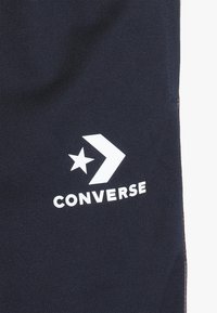 Marineblauwe canvas stof met een wit ster- en pijllogo, met de tekst "CONVERSE" eronder. Gladde textuur en eenvoudig ontwerp.