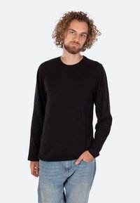 Schwarzes Langarm-T-Shirt aus weichem Stoff, mit Rundhalsausschnitt und lockerer Passform, kombiniert mit hellblauen Jeans.