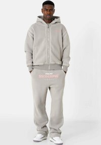 Lichtgrijze hoodie met een ritssluiting aan de voorkant, decoratieve stiksels en een roze logo; bijpassende broek met logo; katoenmix stof; relaxte pasvorm.