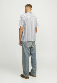 Chemise à manches courtes rayée en tissu léger, avec des rayures verticales navy, un col camp, et une coupe décontractée, associée à un jeans en denim ample.