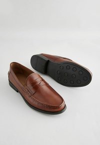 Brune læder loafers med en glat overflade, der har detaljer med stikninger og en fleksibel sort gummisål med cirkulære grebsmønstre.
