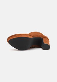 Chaussure à talon haut en daim marron avec un bout lisse et arrondi, et une semelle en caoutchouc noir texturé. Dispose d'un talon profilé pour un soutien supplémentaire.