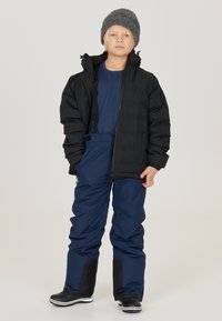 Svart puffjacka, marinblå snöbyxor och svarta stövlar. Barnmodell bär en grå stickad mössa. Strukturerad textil, enhetliga färger, praktisk design.
