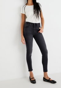 Jeans skinny gris oscuro de cintura alta, combinados con una camiseta ajustada blanca y bailarinas negras con tachuelas blancas. Textura de tela suave.