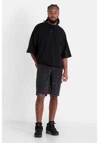 T-shirt nera oversize, pantaloni corti in jeans grigi con orlo grezzo e sneaker alte nere. Stile casual con dettagli minimi e vestibilità rilassata.