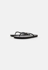 Tongs noires avec deux fines lanières, une semelle intérieure texturée en gris et blanc à motif à carreaux, et une semelle noire légèrement surélevée.