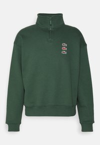 Sweat-shirt vert à demi-fermeture éclair en mélange de coton. Présente un col montant, des poignets côtelés et quatre logos brodés sur la poitrine.