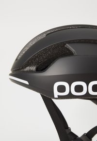 Casco da ciclismo nero con interno testurizzato, forma aerodinamica e branding bianco. Dotato di cinghie regolabili e numerosi canali di ventilazione.