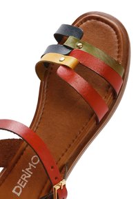 Sandalia de tiras con bandas de cuero en rojo, verde, amarillo y azul. Plantilla texturada en marrón con un detalle de hebilla en tono dorado. Suela plana.