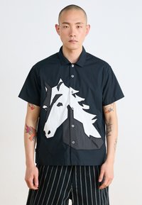 Short-sleeve, black shirt featuring a large, white horse graphic on the front. Fabric has a smooth texture with button closure.
