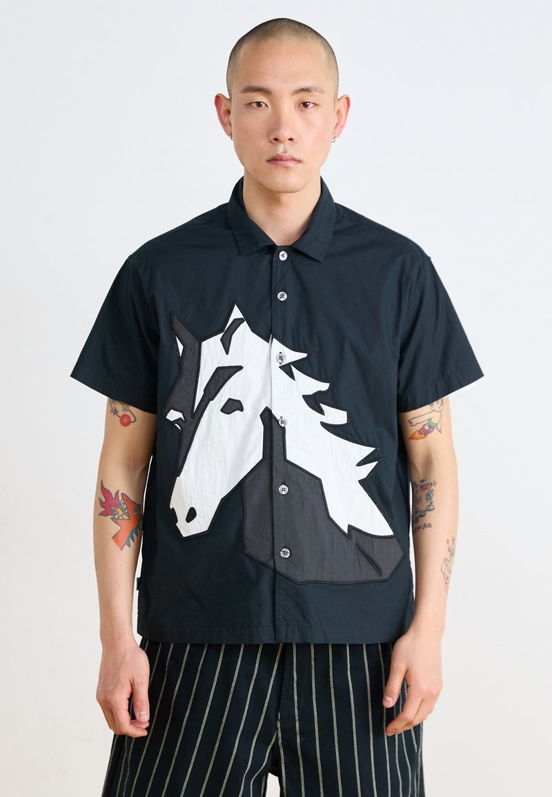 Short-sleeve, black shirt featuring a large, white horse graphic on the front. Fabric has a smooth texture with button closure.