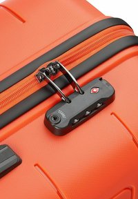Maleta dura naranja con superficie texturizada, presenta un cierre negro y una cerradura de combinación, además de herrajes metálicos en el tirador del cierre.