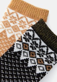 Δύο πλεκτές κάλτσες: η μία σε ζεστό πορτοκαλί με λευκό σχέδιο χιονονιφάδας, και η άλλη μαύρη με σχέδιο διαμαντιού σε λευκό και καφέ, με υφή υφάσματος.