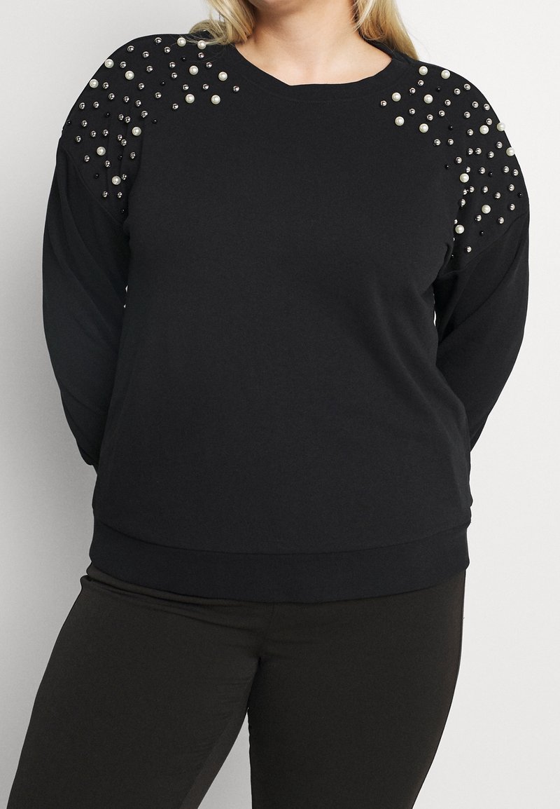 Svart sweatshirt med långa ärmar, prydd med pärlor och metallnitar på axlarna, med rundad halsringning och ribbat avslut.