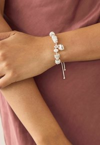 Srebrna bransoletka z naprzemiennie umieszczonymi białymi perłami i dekoracyjnymi koralikami, z przesuwanym zapięciem oraz zwisającymi metalowymi akcentami.
