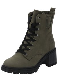Botas de tobillo verde militar con una textura suave, frontal con cordones negros, tacón grueso y suela negra rugosa. Detalle de marca visible en el lateral.