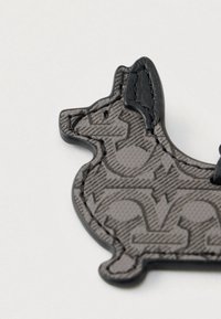 Γκρι και μαύρο δερμάτινο μπρελόκ σε σχήμα καθισμένου σκύλου με ραφές στο λευκό φόντο.