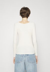 Maglietta a maniche lunghe, aderente, in tessuto a maglia color crema, con scollatura rotonda e texture liscia, abbinata a jeans blu chiaro a vita alta.