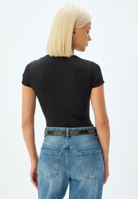 Sort kortærmet tætsiddende top parret med højtaljede lysblå denimjeans. Outfittet har et dekorativt sort bæltet med nitter.