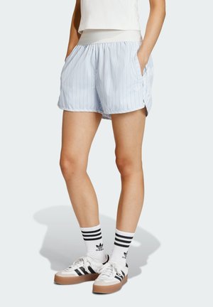 Világoskék csíkos rövidnadrág gumis derékrésszel, oldalzsebekkel és laza szabással, fehér és fekete tornacipővel, valamint csíkos zoknival párosítva.