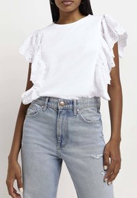 Vit bomull t-shirt med ögonlapp spets volangärmar, matchad med ljusblå högmidjade jeans med lätt slitningar och framknapp.