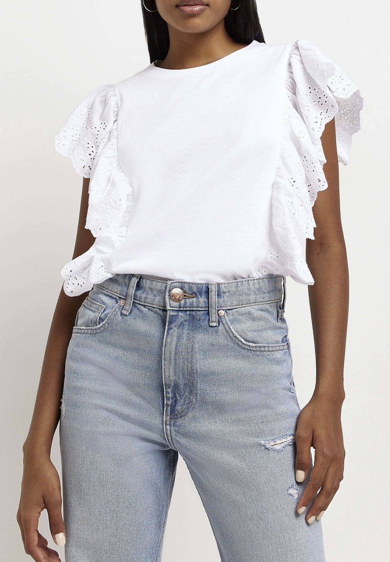 Vit bomull t-shirt med ögonlapp spets volangärmar, matchad med ljusblå högmidjade jeans med lätt slitningar och framknapp.