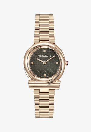 Reloj de oro rosa con caja redonda, esfera negra texturizada que presenta marcadores de hora en forma de cuadrado y una pulsera de eslabones de metal. Destalle rojo en la corona.